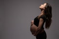 Side view portrait of the beautiful pregnant woman with loose hair that looking up and holds hands on her swollen belly Royalty Free Stock Photo