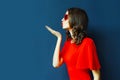 side view portrait beautiful young woman blowing red lips sending sweet air kiss wearing heart shaped sunglasses on blue wall Royalty Free Stock Photo