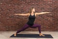 Side view portrait of beautiful young woman wearing black top and purple leggings working out against brick wall, doing yoga or Royalty Free Stock Photo