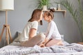 Side view portrait of brown haired woman and little girl, mother and daughter sitting in bed with closed eyes touching noses Royalty Free Stock Photo