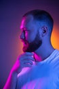 Close up portrait of young caucasian bearded man  on dark studio background in neon lights. Side view Royalty Free Stock Photo