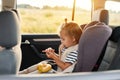 Side view portrait of cute charming baby girl sitting in a car in safety chair, playing alone, holding bananas, wearing striped t Royalty Free Stock Photo