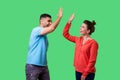 Side view portrait of excited amazed young couple in casual wear giving high five. isolated on green background