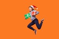 Side view portrait of extremely joyous brunette woman in santa hat jumping or running in air with wrapped xmas gift boxes, Royalty Free Stock Photo