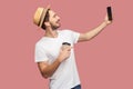 Side view portrait of handsome bearded young hipster man in white shirt and casual hat posing and making selfie photo with smile, Royalty Free Stock Photo