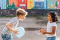 Side view portrait of happy little blond boy giving blue balloon for cute little hispanic curly preschool girlfriend, outdoor. Royalty Free Stock Photo