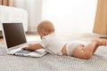 Side view portrait of little infant baby girl wearing white t shirt playing with laptop while lying on floor in living room Royalty Free Stock Photo