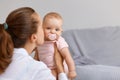 Side view portrait of lovely woman with dark hair woman playing with her infant daughter at home, mother kissing her baby, Royalty Free Stock Photo