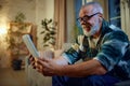 Side view portrait of mature man in glasses sitting on couch in living room and watching movie in tablet and in Royalty Free Stock Photo