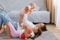 Side view portrait of mom and sweet child girls lying and playing on floor, mother holding infant baby ina hands, family Royalty Free Stock Photo