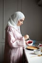 Side view portrait Muslim woman cooks dessert cake at kitchen, arabian young model in hijab and abaya. Islamic