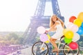 Girl cycling through Paris with balloons bouquet