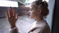 Side view portrait of sad brokenhearted teenage girl looking out the window on rainy day touching glass. Depressed