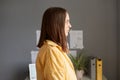 Side view portrait of serious assertive young adult woman with brown hair wearing yellow shirt posing in office, looking ahead Royalty Free Stock Photo