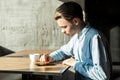 Side view portrait of serious attentive young businessman in denim blue shirt sitting using phone