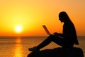 Silhouette of a woman using laptop at sunset