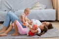 Side view portrait of smiling optimistic woman lying on floor with her daughters, baby kid sitting on mom`s belly, elder child Royalty Free Stock Photo