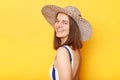 Side view portrait of smiling woman wearing striped swimming suit and sun hat isolated on yellow background looking at camera with Royalty Free Stock Photo