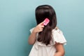 Side view portrait of teenager girl in white dress standing, making attention and combing brunette hair with pink hairbrush.