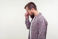 Side view portrait of unhappy bearded man in casual plaid shirt standing with head down, rubbing eyes and crying. white background Royalty Free Stock Photo