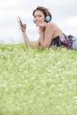 Side view portrait of woman listening to music through cell phone using headphones while lying on grass against sky Royalty Free Stock Photo