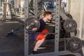 Side view portrait of young adult bodybuilder are workout in gym alone and prepearing to lifting barbell, doing exercises for legs Royalty Free Stock Photo