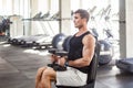 Side view portrait of young adult man muscular built handsome athlete working out in a gym, sitting on bench and holding two Royalty Free Stock Photo