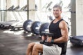 Side view portrait of young adult man muscular built handsome athlete working out in a gym, sitting on a weightlifting machine and