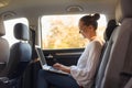 Side view portrait of young business woman using laptop computer while sitting in the back seat of car, typing on portable Royalty Free Stock Photo