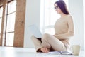 Side view portrait of young charming smiling woman in glasses sitting on the floor at home and holding laptop on her Royalty Free Stock Photo