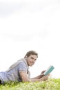 Side view portrait of young man holding book while lying on grass against clear sky Royalty Free Stock Photo