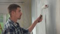 Side view of a portrait of a young man is painting wall with white paint using a paint roller. Male painter in checkered Royalty Free Stock Photo