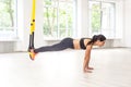 Side view portrait of young muscular woman wearing black top and leggings standing on plank position use fitness straps, doing Royalty Free Stock Photo