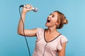 Side view positive blonde woman in summer dress loudly singing song, holding microphone in hand, having fun resting in karaoke,