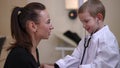 Side view positive curios little boy using stethoscope talking with young beautiful woman. Charming cute Caucasian son