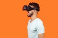 Side view of positive gamer, brunette man watching video or playing virtual reality game. isolated on orange background Royalty Free Stock Photo