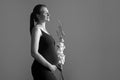 Side view pregnant woman with flower holds hands on belly monochrome foto. Young woman in dress waiting for baby birth Royalty Free Stock Photo