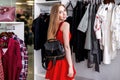 Side view of pretty girl wearing red set doing shopping alone choosing, holding, examining new bag in fashion store Royalty Free Stock Photo