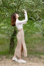 Pretty, slim girl standing, bending blooming tree branch, smelling, looking up, admiring. Royalty Free Stock Photo