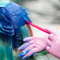 Side view of process of dyeing hair in stylish color. Hairdresser in pink glove using magenta brush while applying blue