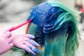 Side view of process of dyeing hair in unique color. Hairdresser in glove using pink brush while applying blue paint to