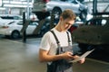 Side view of professional handsome young mechanic male wearing uniform holding clipboard and using texting mobile phone Royalty Free Stock Photo