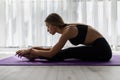 Side view of a woman exercising and stretching her body doing flexibility exercises and bending her back, sitting on a yoga mat Royalty Free Stock Photo