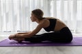 Side view of a woman exercising and stretching her body doing flexibility exercises and bending her back, sitting on a yoga mat Royalty Free Stock Photo