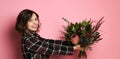 Side view profile of attractive young woman in a dark checkered dresst holding bouquet of flowers and giving you. Royalty Free Stock Photo