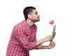 Side view profile portrait of handsome bearded young man in red checkered shirt standing and holding one tulip flower and smiling Royalty Free Stock Photo
