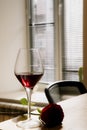 side view of red color rose lying near a glass of red wine on a wooden table at window background Royalty Free Stock Photo