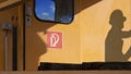 Side view of red fire extinguisher sign on train head door with sunlight and shadow of engineer on surface of orange train wall