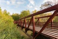 Side view of a red iron pedestrian bridge of a greenway surrounded by trees running over a river on the Neuse River Greenway in