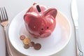 Side view of a red piggy bank on a plate with cutlery. Eat savings, consumer savings concept, eating savings. Consumer savings